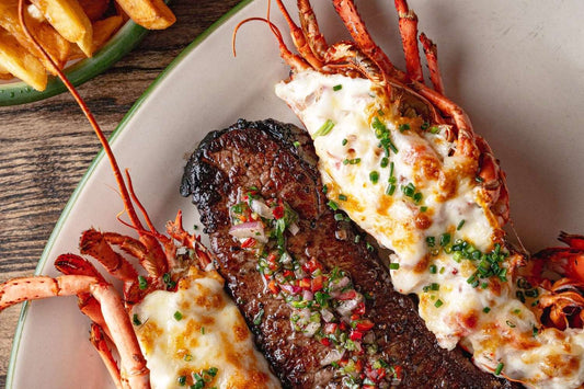 Lobster tail with creamy sauce and garnishes on a plate with fries in the background.